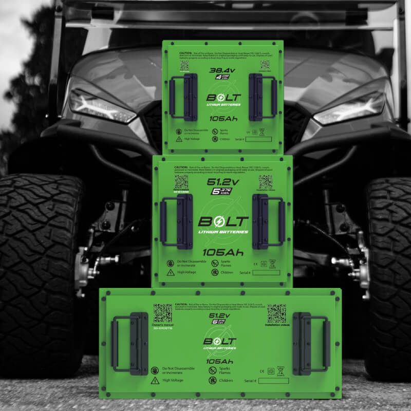 Three Bolt lithium golf cart batteries stacked in front of a golf cart